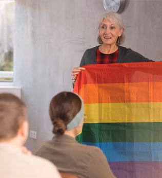 Photo of a speaker holding up a rainbow flag to her audience