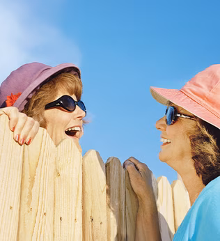 Photo of two woman talking over a wooden picket fence