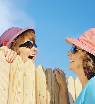 Photo of two woman talking over a wooden picket fence