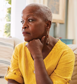 Photo of a woman in a yellow top resting her chin on her hand