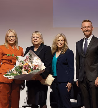 Photo of four lawyers on stage with a large bouquet