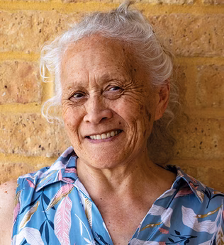 Photo of a smiling woman with a cream brick wall in the background