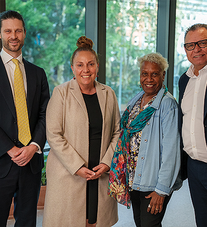 Photo of a group of four people wearing business casual clothes smiling at the camera