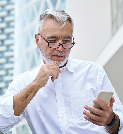Photo of a man with a white beard and shirt looking at his phone