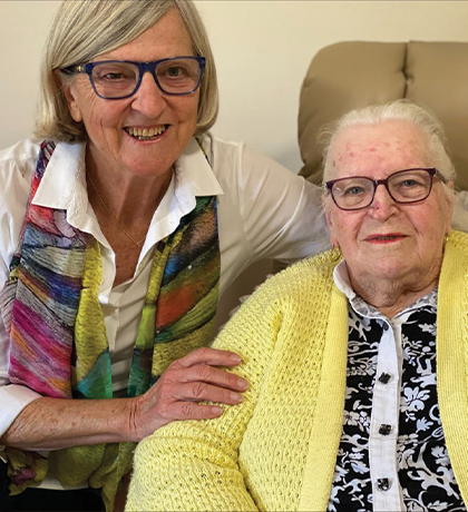 Photo of a woman with a colourful scarf embracing another in a yellow cardigan