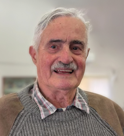 Photo of a smiling man in a taupe and grey jumper