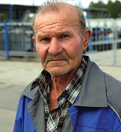 Photo of man in blue and grey standing in front of a fence