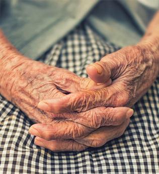 Photo of old and hardworking hands clasped on a green gingham skirt