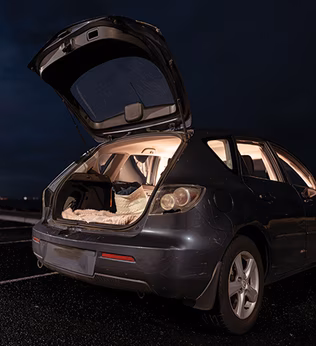 Photo of a car at night with a bed visible through the open rear hatch