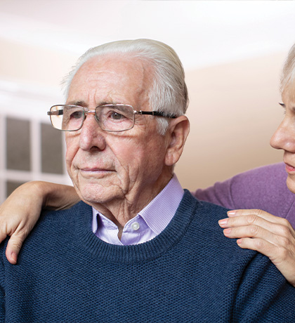 Photo of a woman in a lavender cardigan comforting a man with glasses