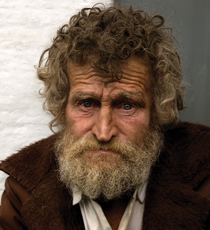 Photo of a man with curly brown hair and a brown jacket