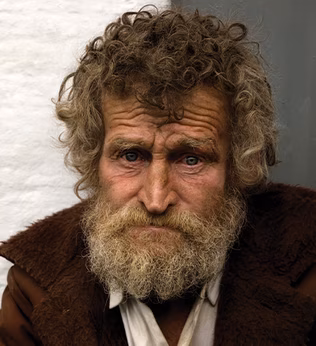 Photo of a man with curly brown hair and a brown jacket