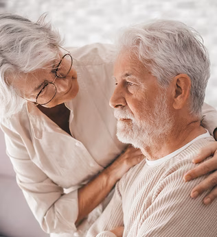 Photo of a woman in white embracing the shoulders of a man in cream