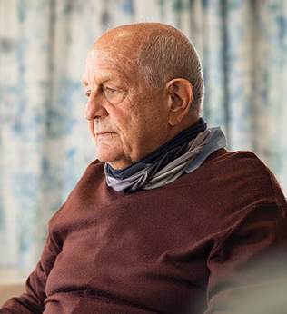 Photo of a man in a chocolate brown jumper holding a paper coffee cup