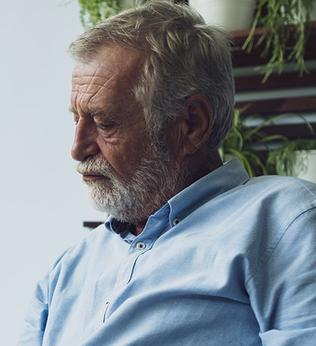 Photo of sad man with a white beard sitting near a garden