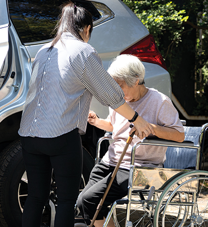 Photo of a person in a wheelchair being helped into a car