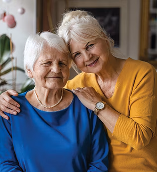 Photo of two smiling women with a vase of pink flowers