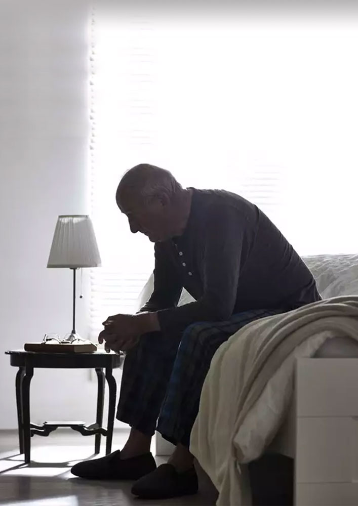 Older man sitting despondently on the side of a bed