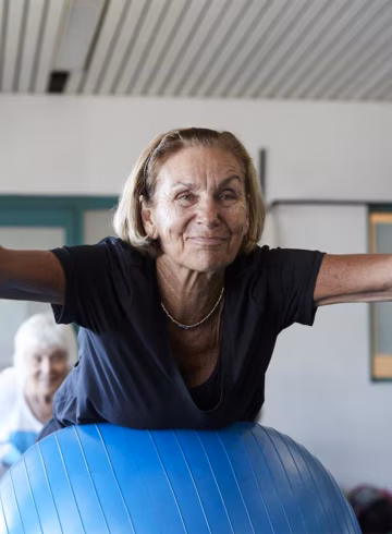 Image of an older woman exercising indoors with a group of older woman