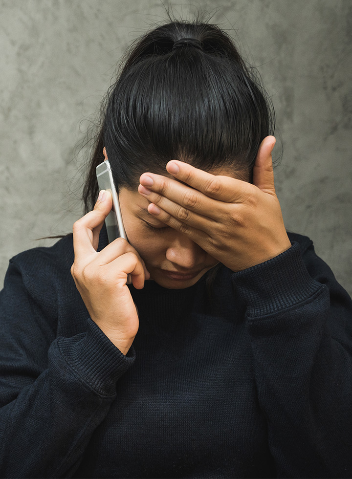 Image of a woman with her left hand holding her forehead and her right with a mobile phone to her ear