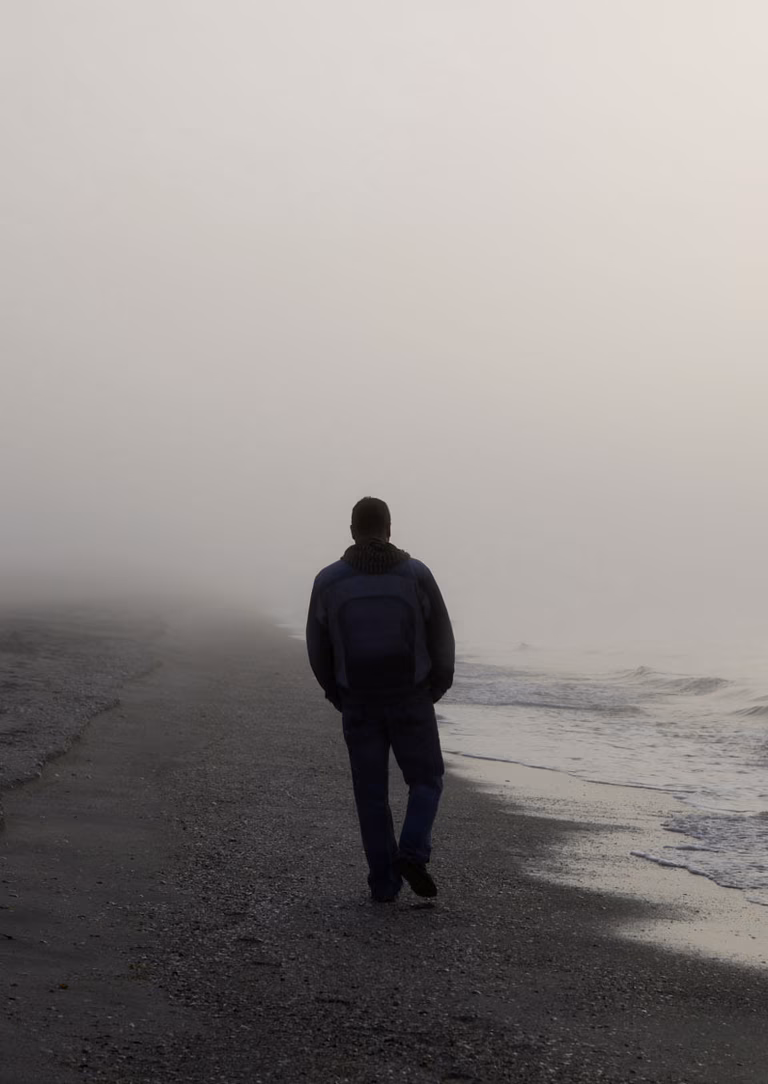 Mann, der an einem nebligen Morgen am Strand spazieren geht 