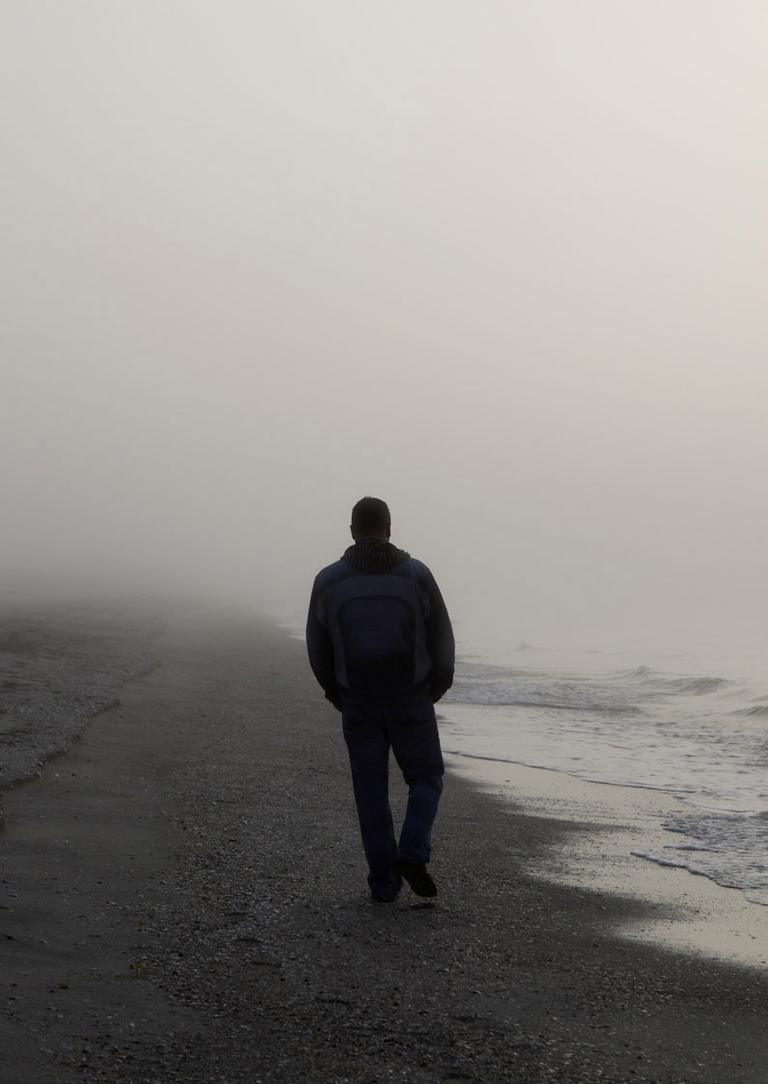 Hombre caminando por la playa en una mañana de niebla 
