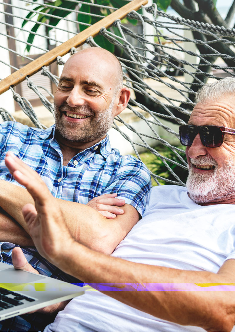 Two older men in a hammock looking at a laptop computer