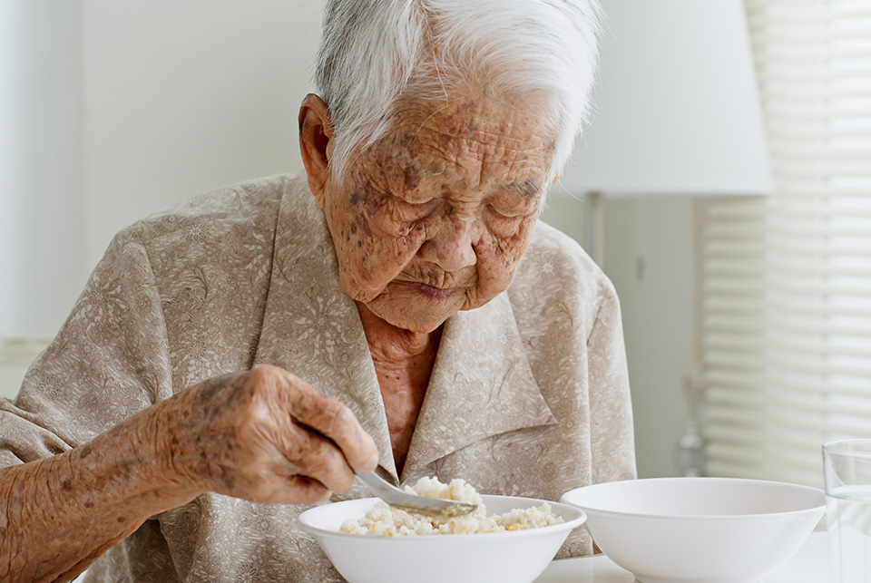 Photo of older Asian woman eating a bowl of rice