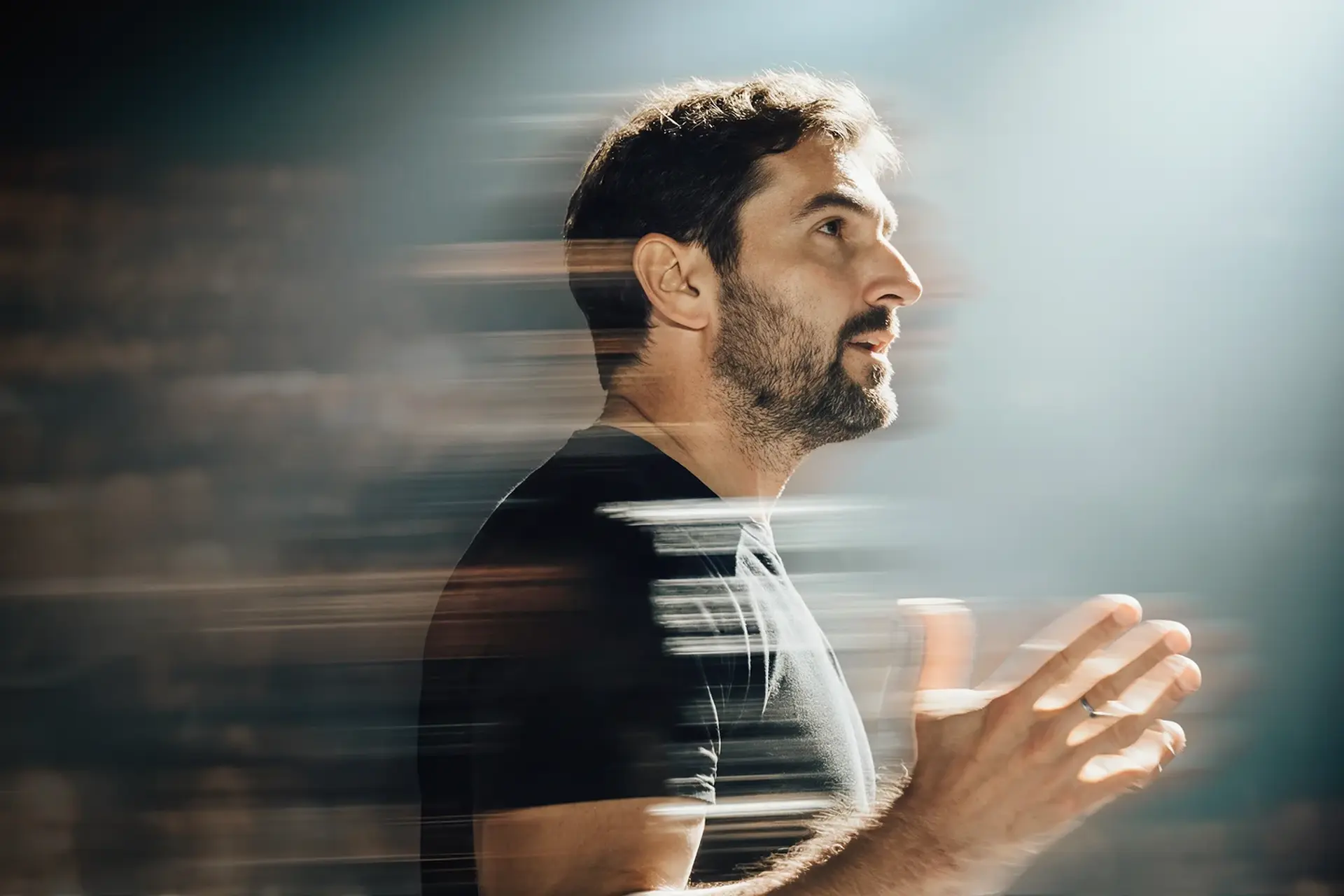 Man in a black shirt speaking passionately, with a dynamic motion blur effect, under soft light.