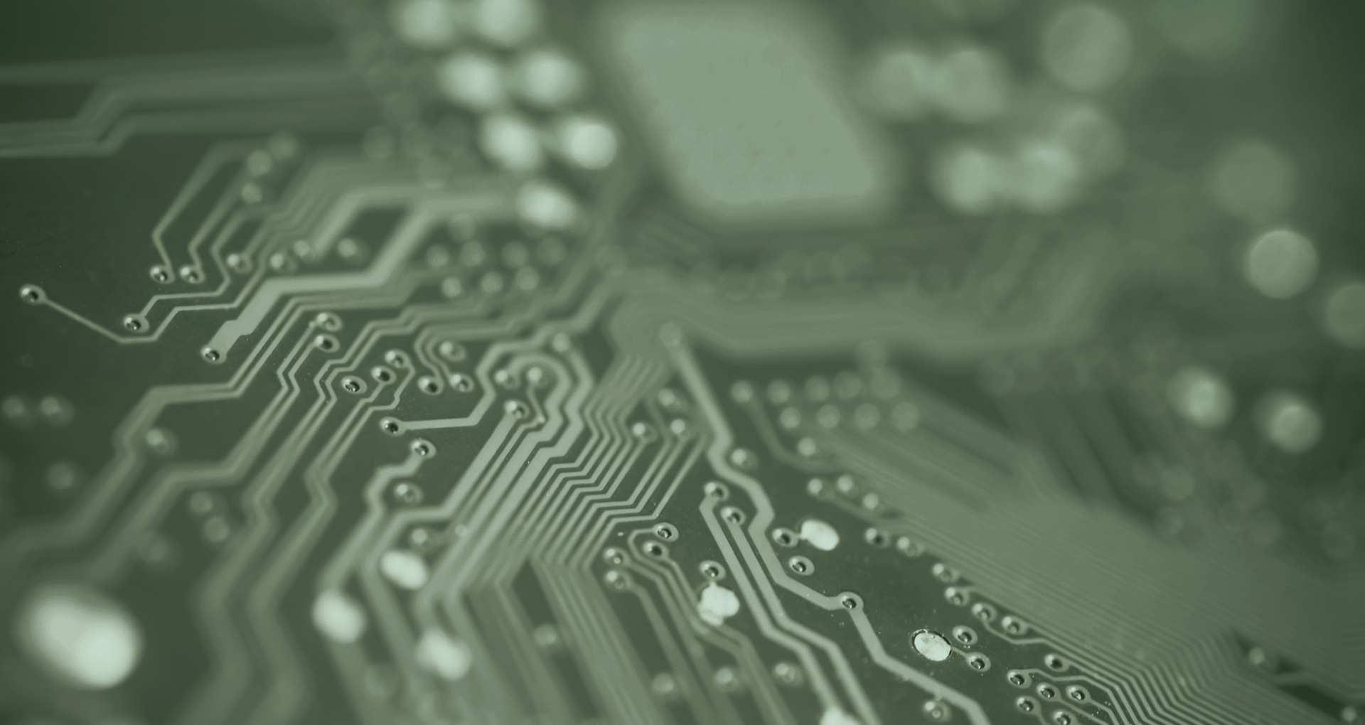 Close-up of a green circuit board with intricate pathways and soldered connections, showcasing electronic components and circuitry patterns.
