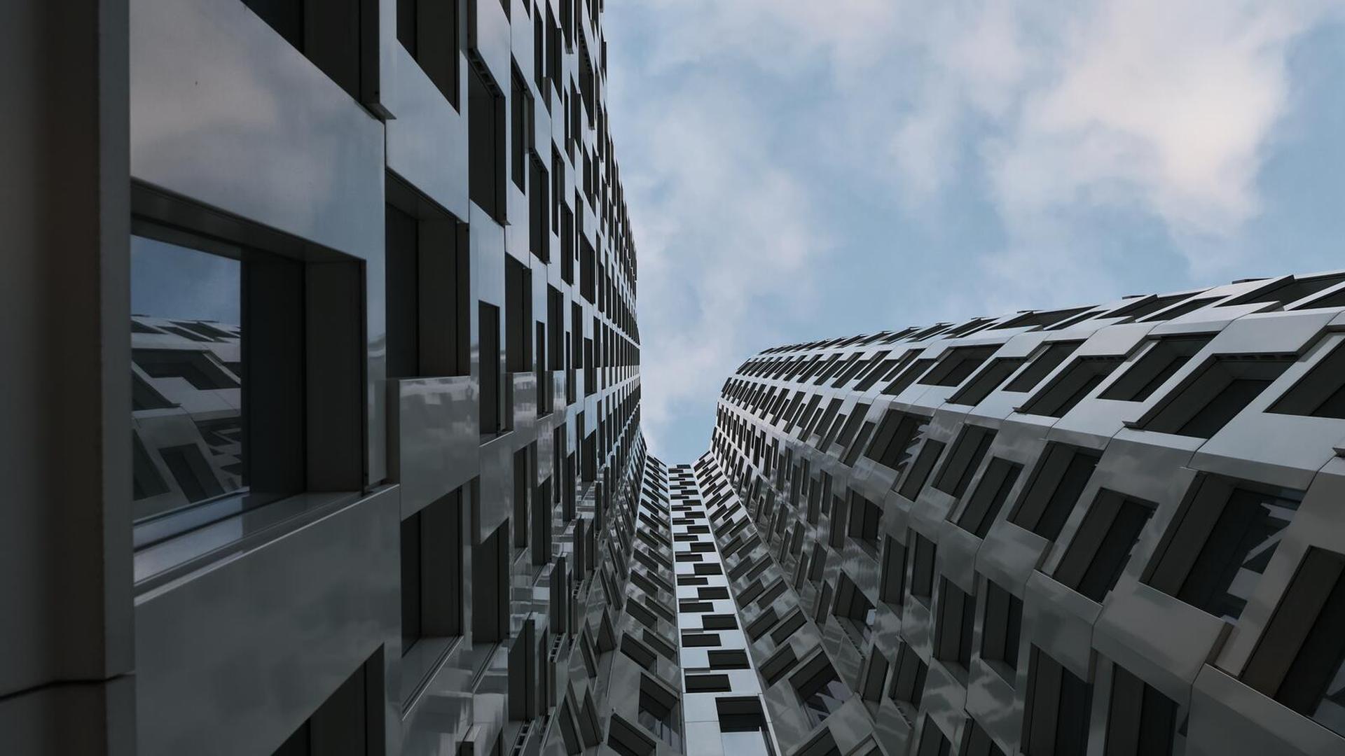 Looking up between two modern, reflective buildings with geometric patterns, set against a clear blue sky.