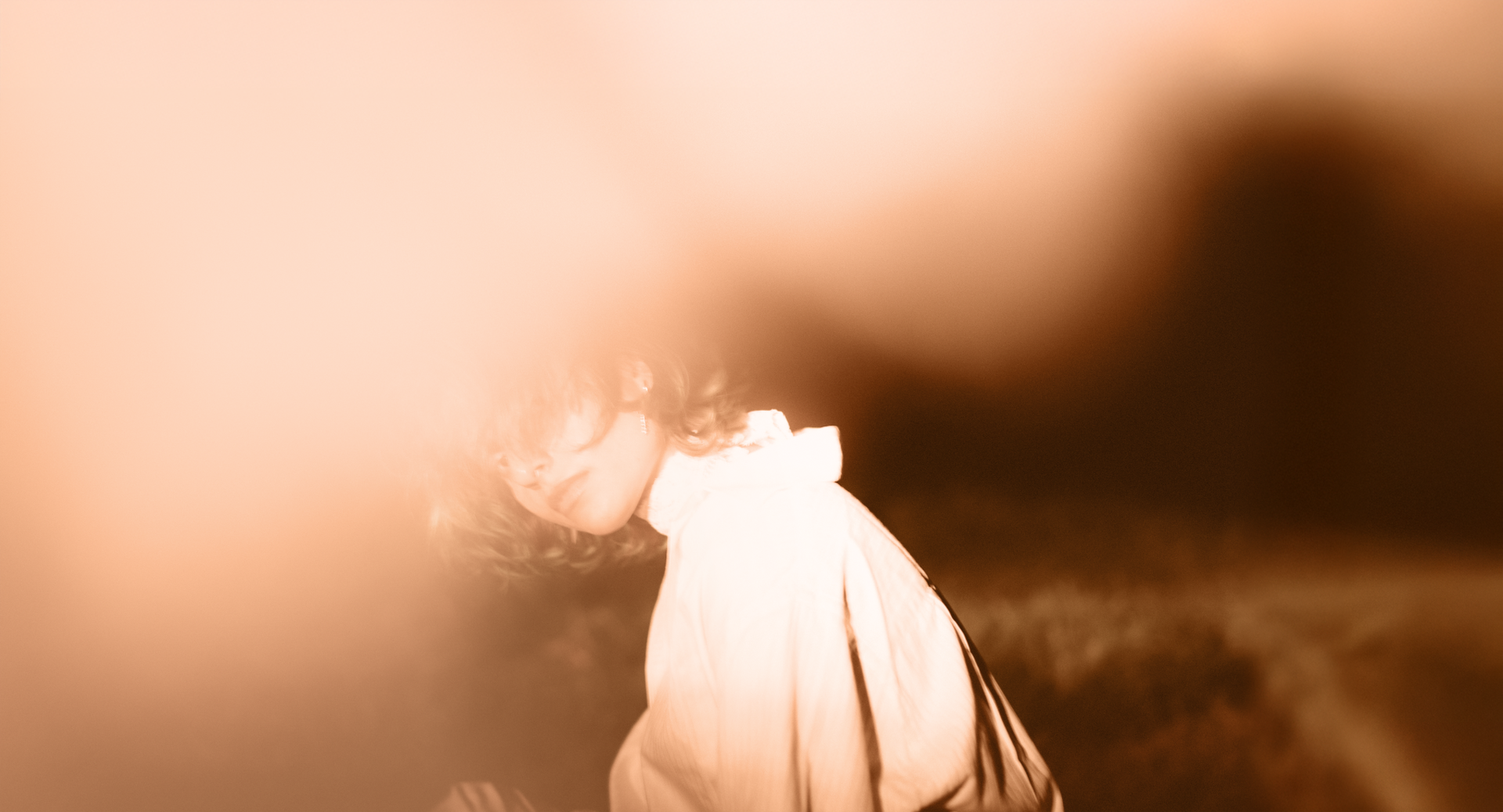 A person in a white shirt partially obscured by a soft, warm blur, creating a dreamy and ethereal atmosphere.