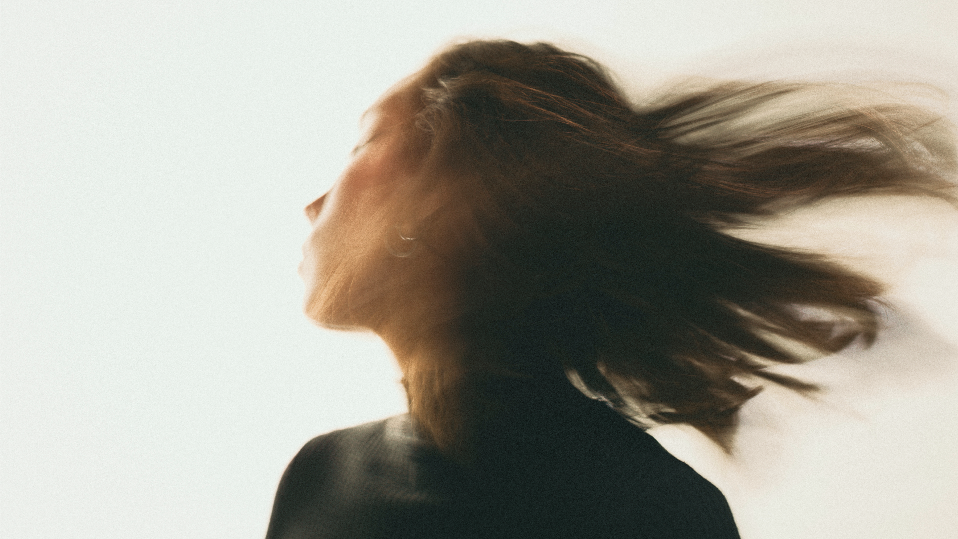 Blurred side profile of a person with long hair, captured mid-motion against a light background.