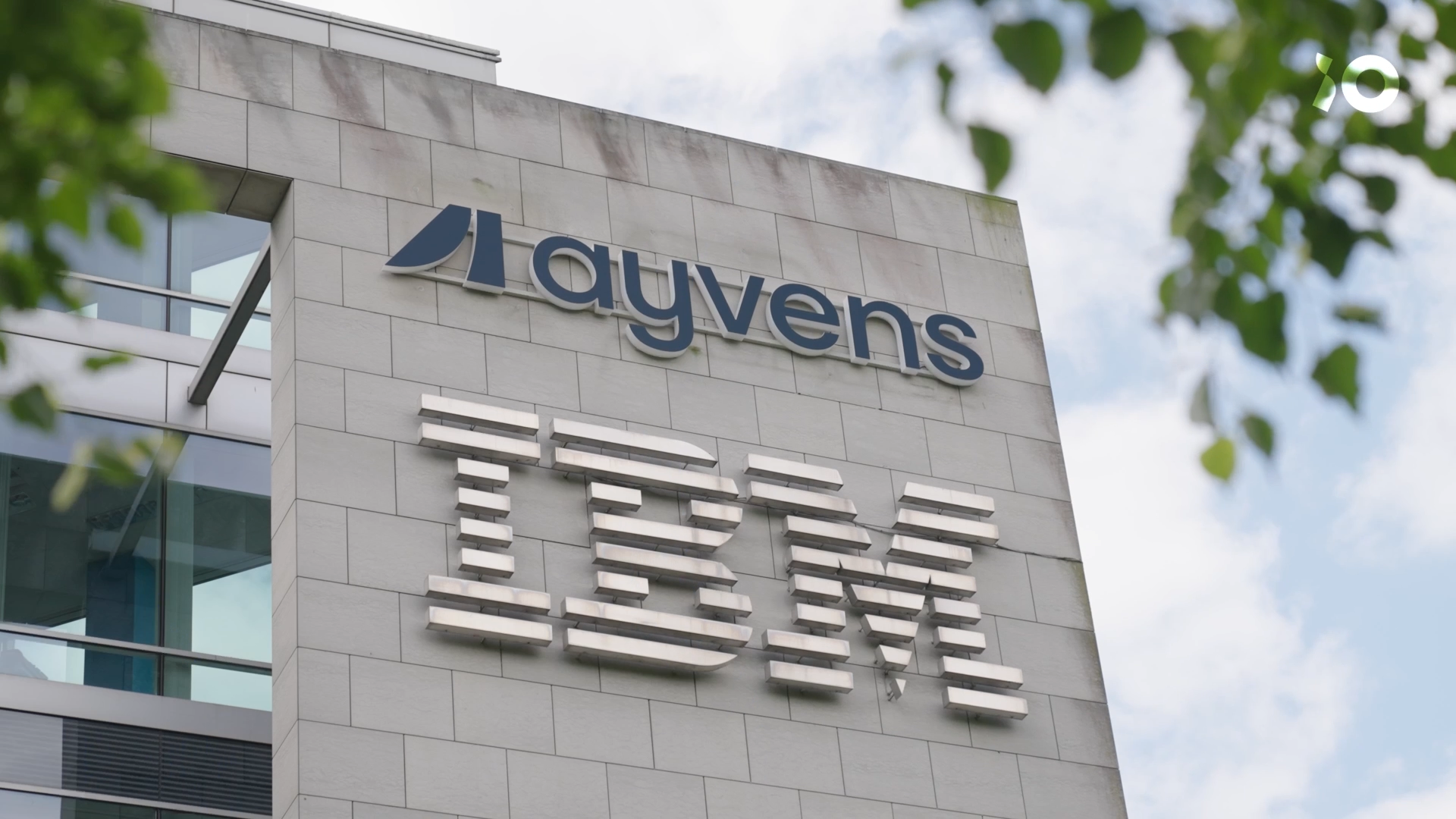 Building facade with IBM and "ayvens" logos. The sky and some green leaves are visible in the background.