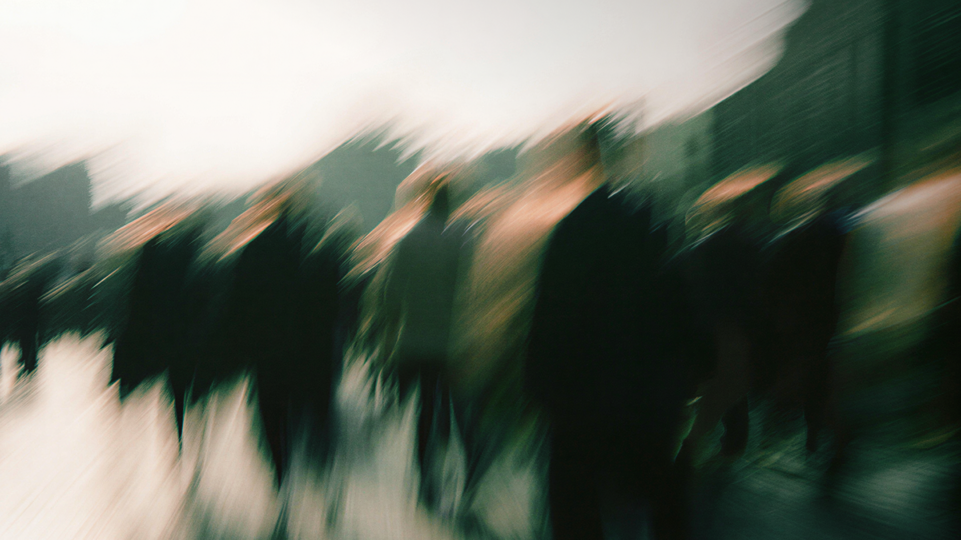 Blurred image of people walking in a cityscape, creating a dynamic abstract effect with motion and indistinct figures.