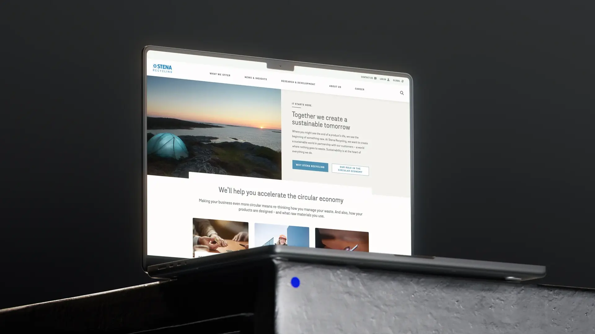 Laptop displaying a webpage about creating a sustainable tomorrow, with an image of a tent by the sea at sunset, on a gray background.