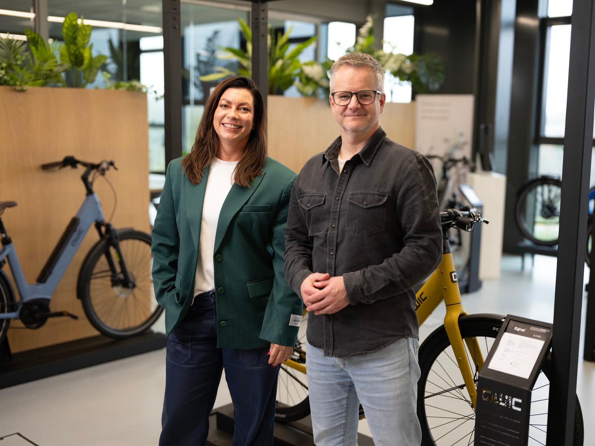 Carolin Wenk and Maurice van der Beek smiling and standing in a modern bicycle shop with bikes displayed around them.