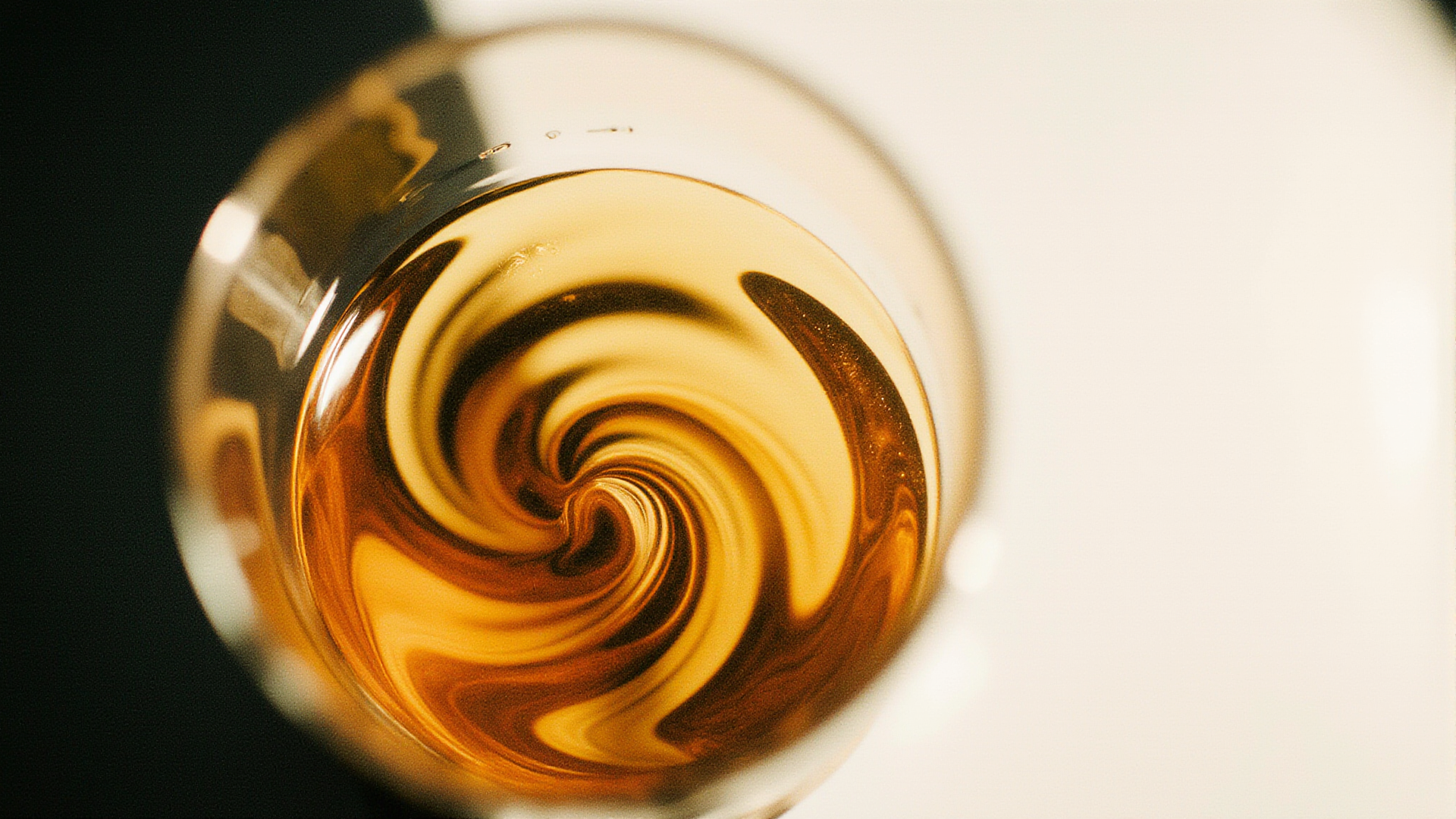 Top view of a swirling amber liquid in a glass against a blurred black and white background.