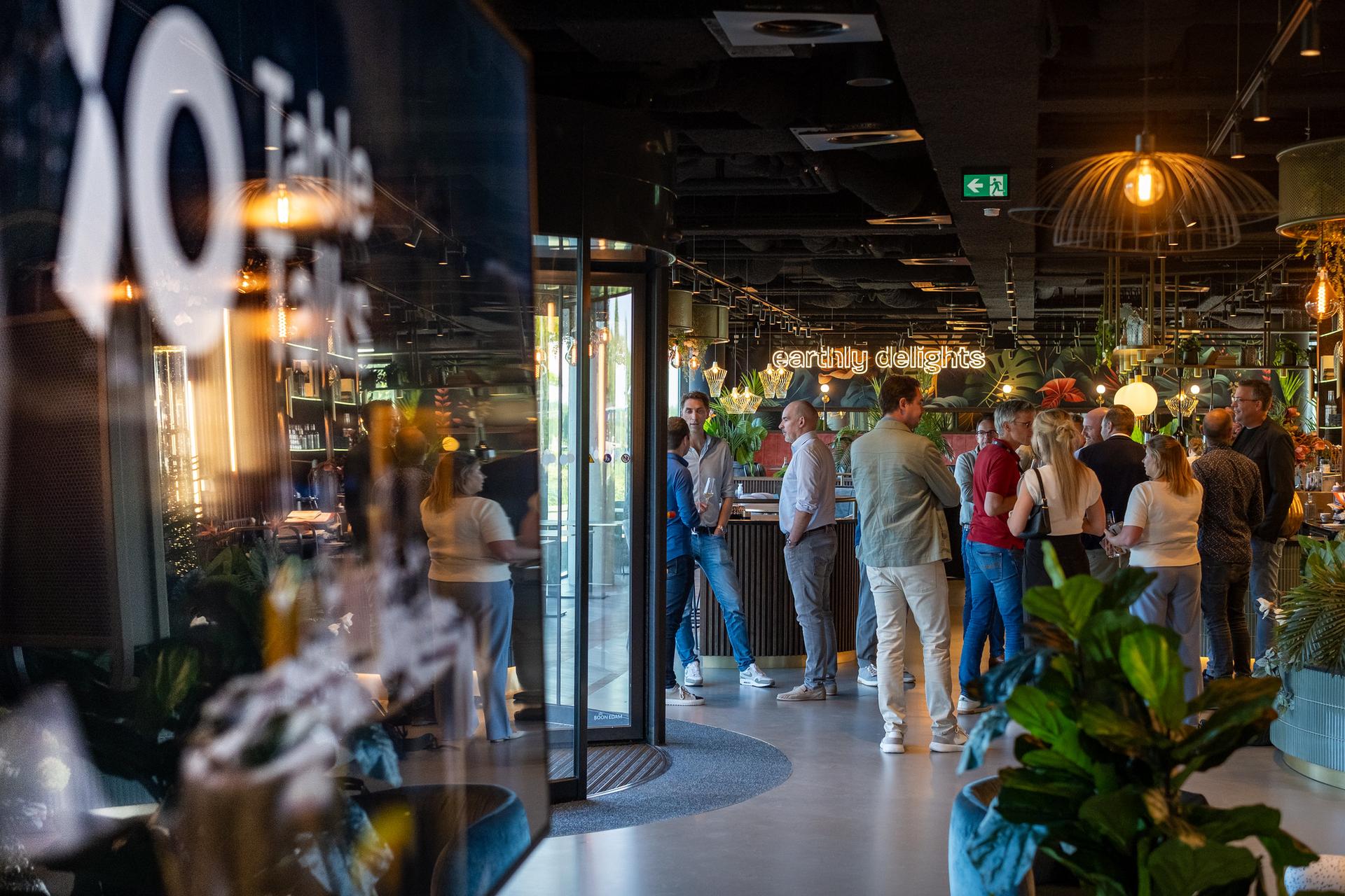 A group of people gathered in a modern, stylish indoor space with plants and ambient lighting. A sign reads "candidly delightful."