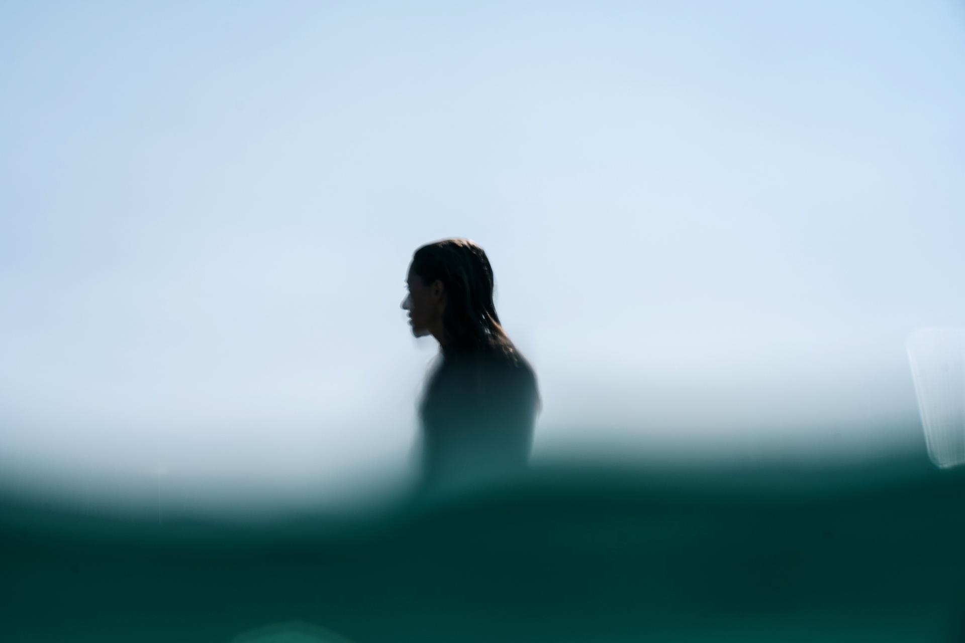 Silhouetted person partially submerged in water against a clear sky, creating a serene and mysterious ambiance.