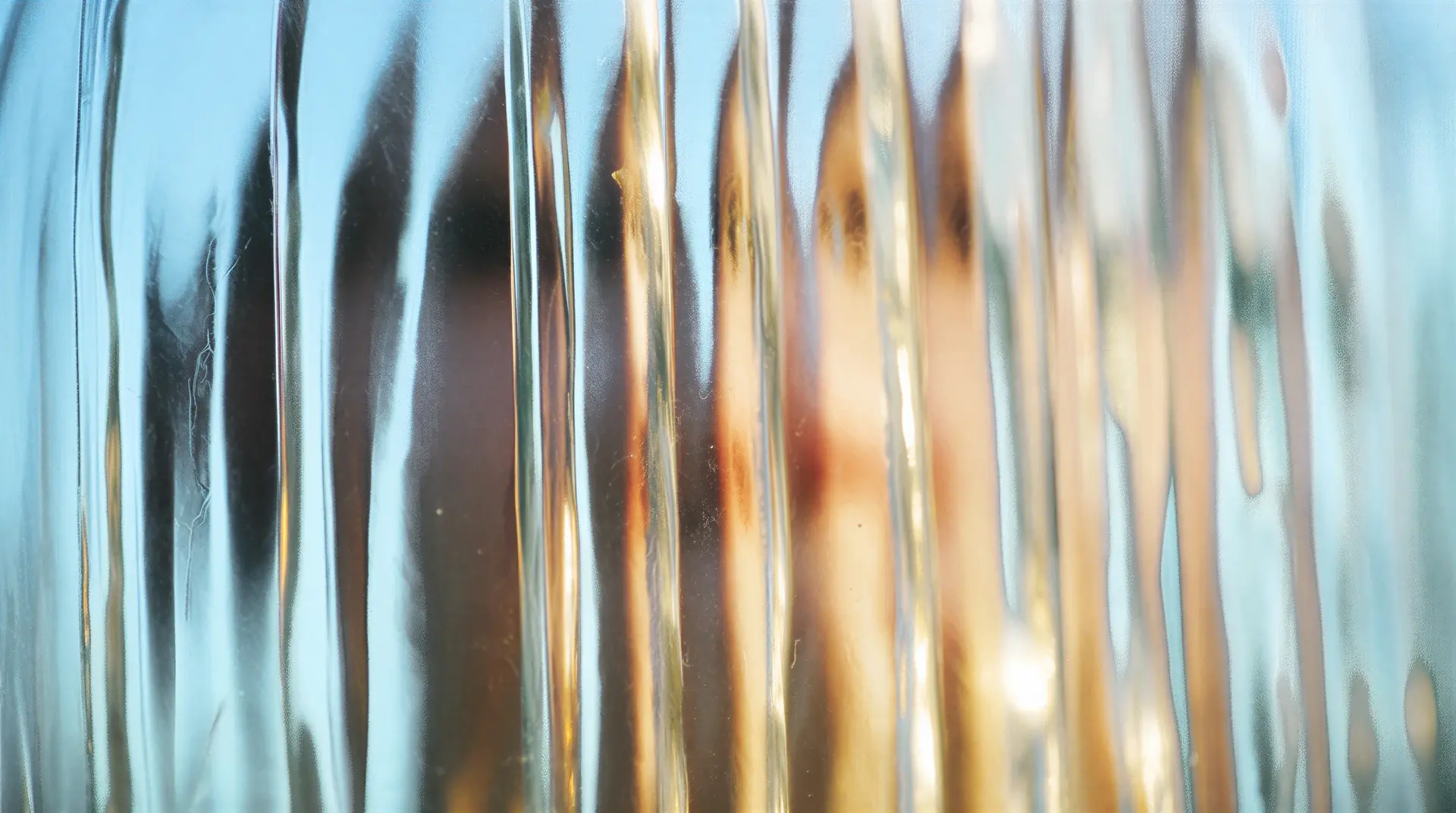 Abstract image with vertical glass streaks, distorting light and colors of blue, gold, and orange, creating a blurred effect.