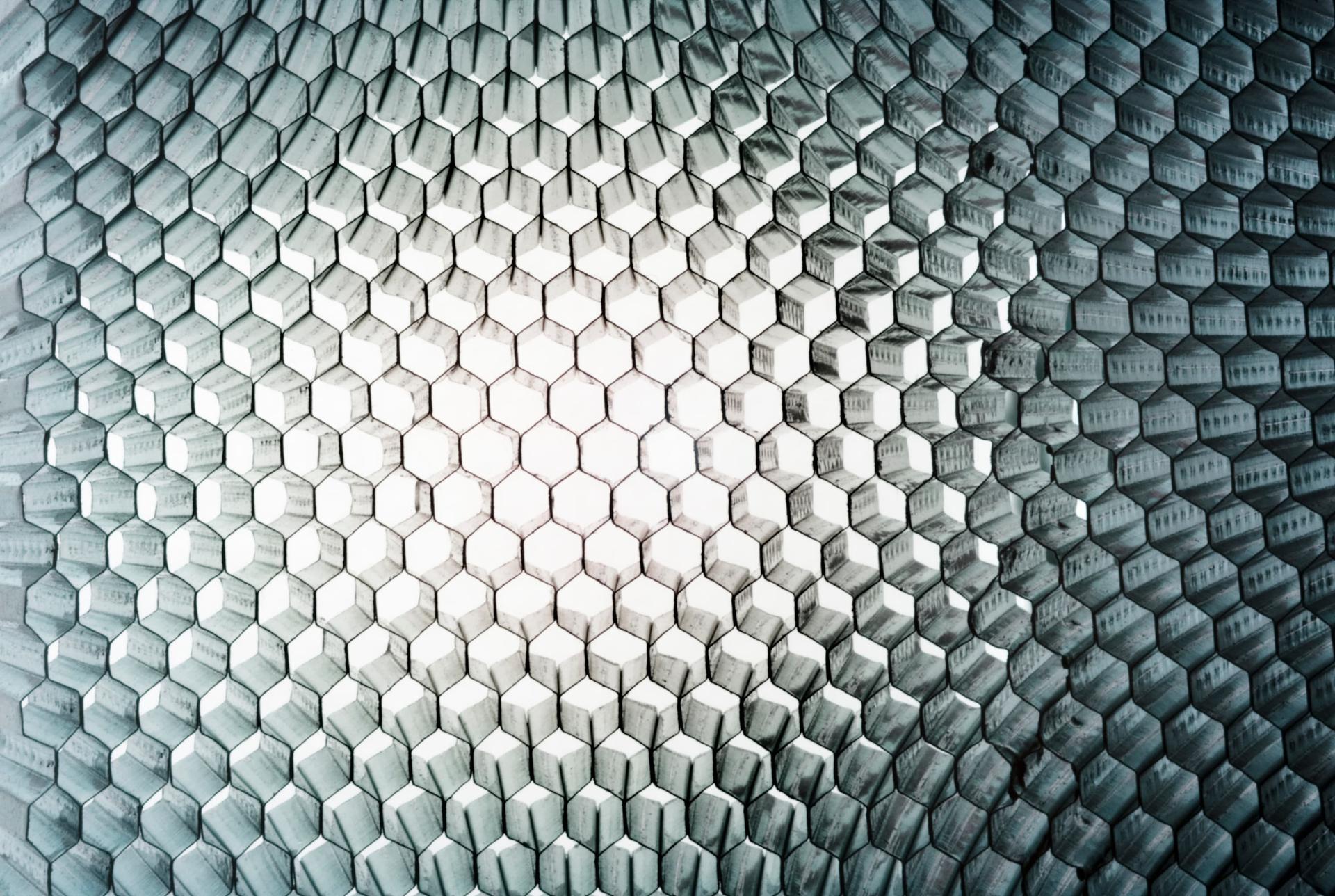 Geometric pattern of interlocking hexagons in shades of gray, creating a textured, three-dimensional effect with a central light gradient.