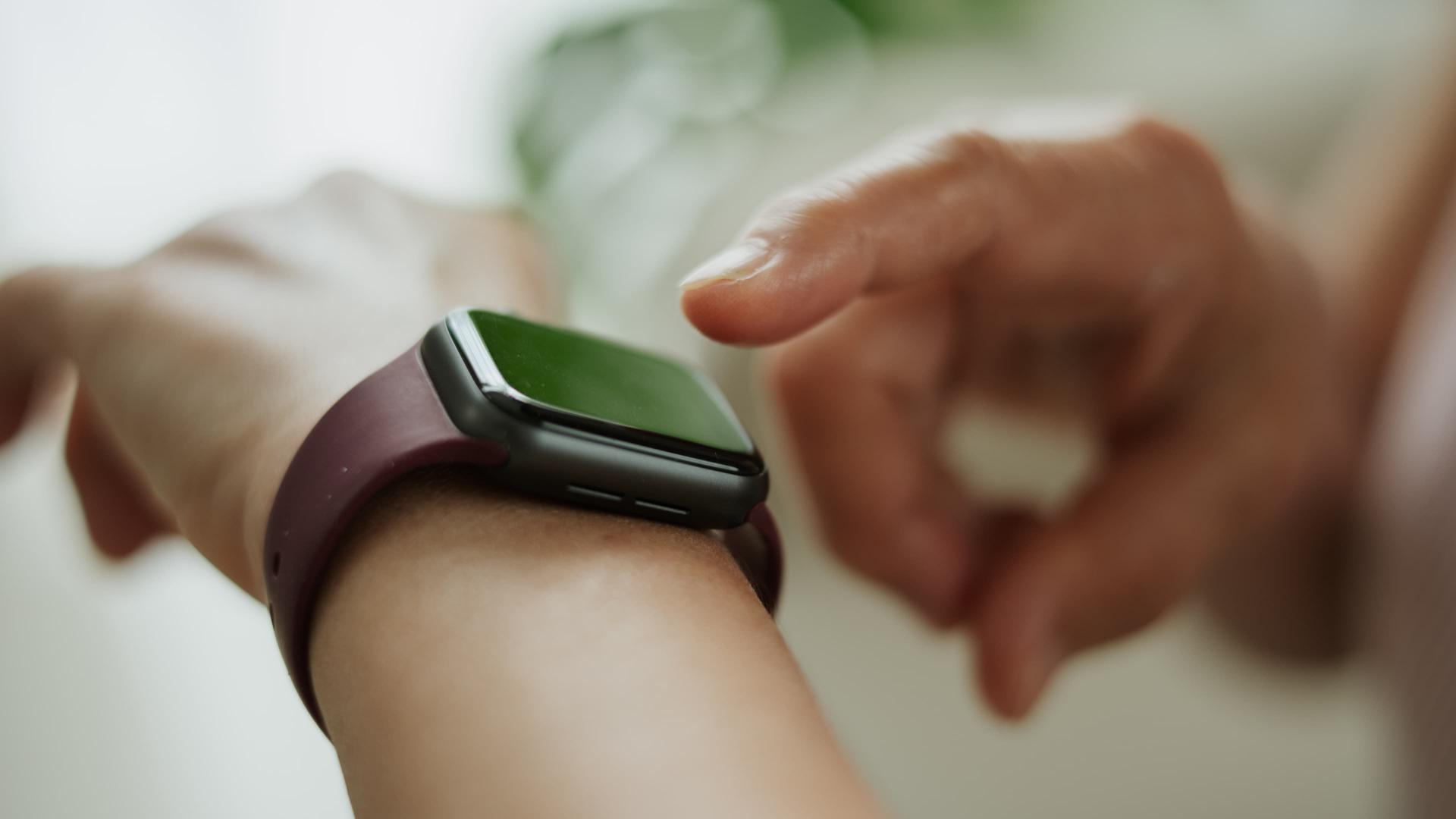 Person interacting with a smartwatch on their wrist, tapping the screen with a finger. The watch has a maroon band.