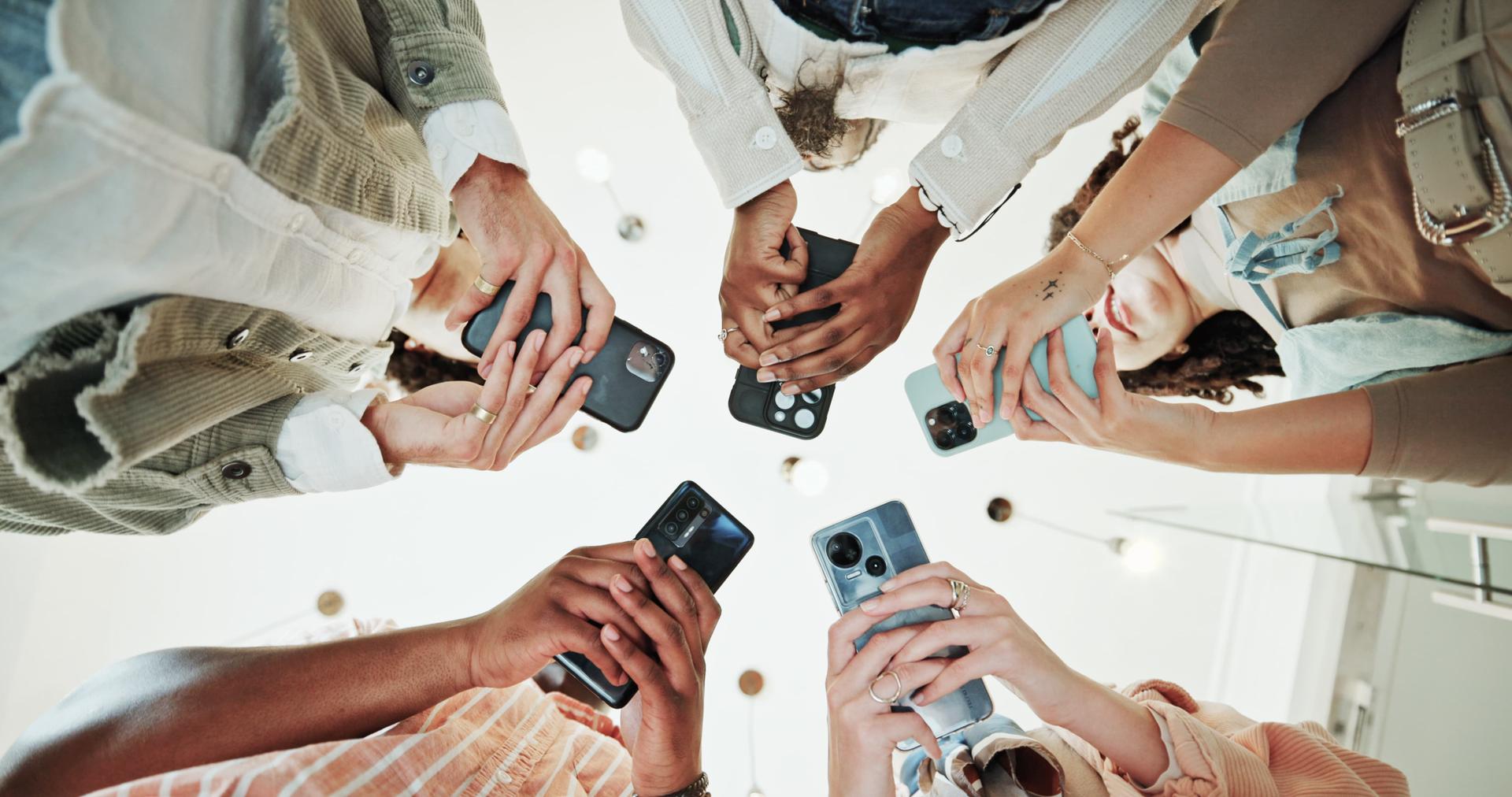 A group of people standing in a circle, holding smartphones, viewed from below.