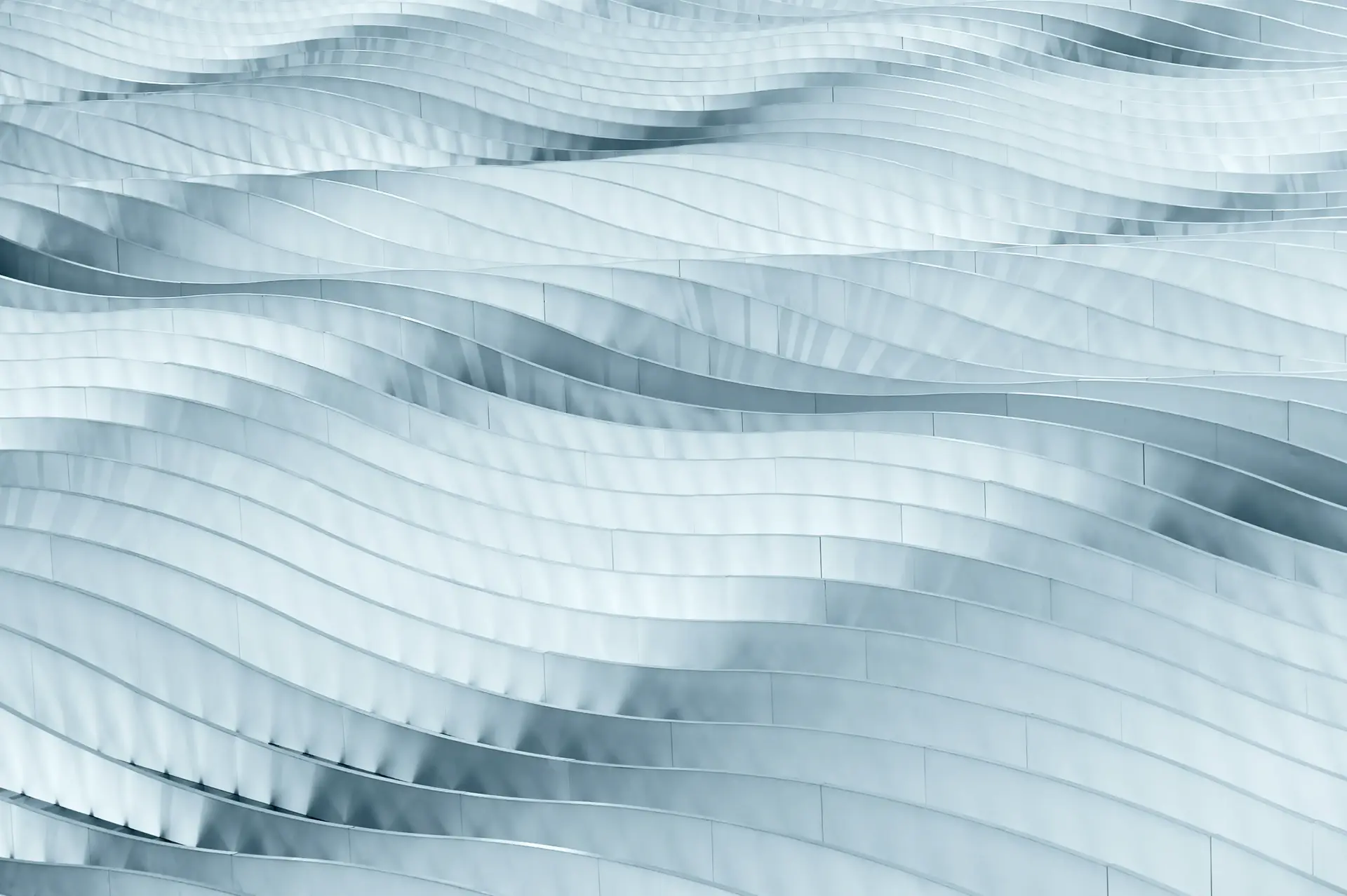 Abstract pattern of wavy, metallic-like surfaces with a smooth, flowing texture in shades of light blue and gray.