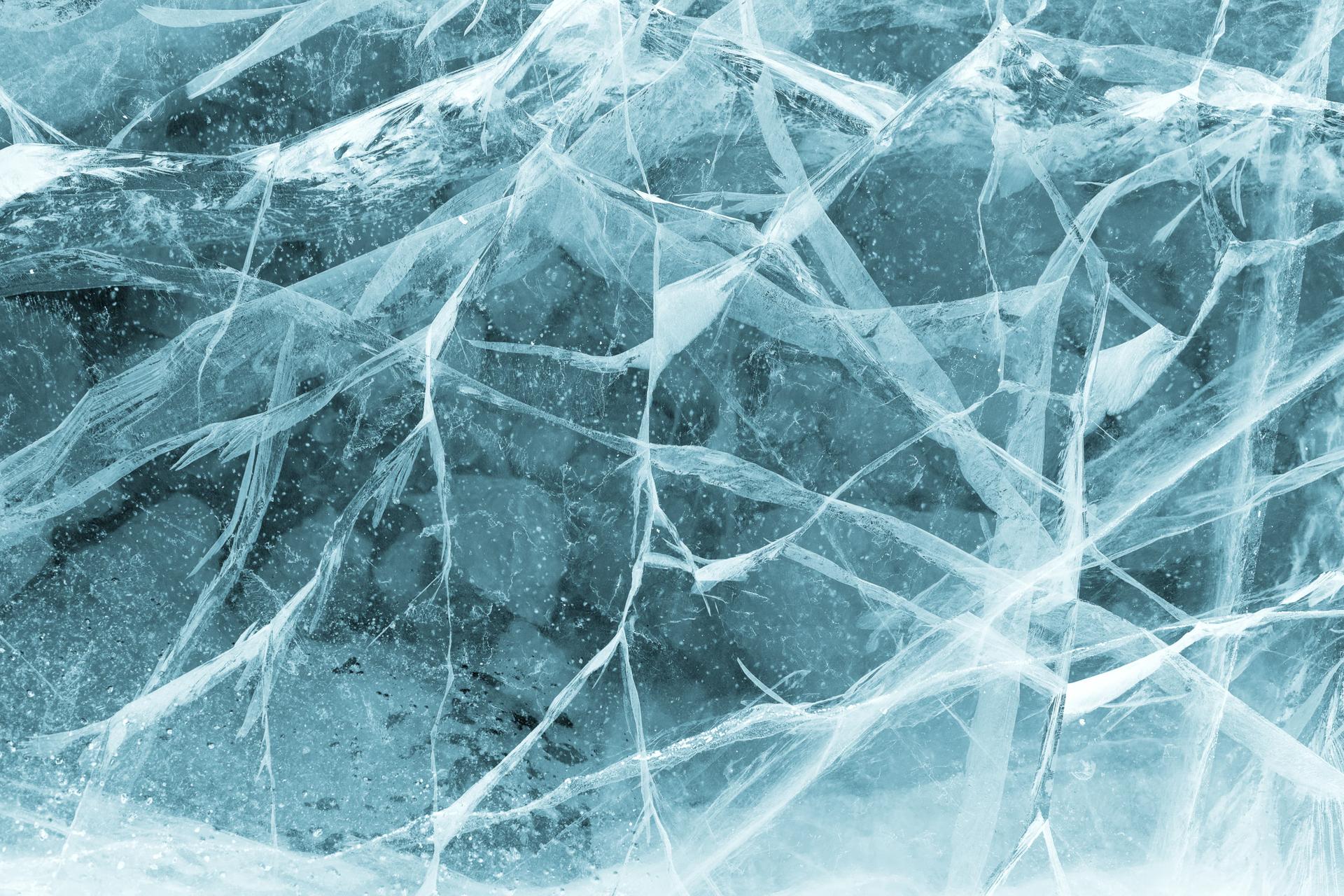 Close-up of cracked ice with intricate patterns and a blue tint, highlighting the texture and complexity of the frozen surface.