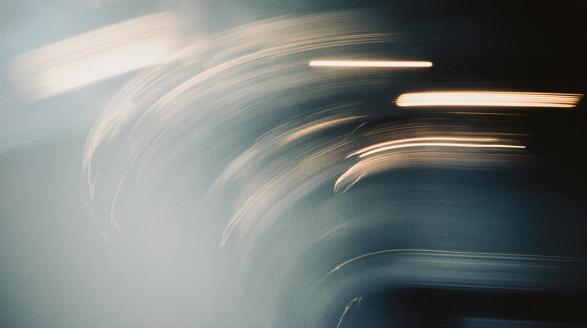 Abstract image with swirling light trails in shades of blue and orange, creating a dynamic and ethereal effect.