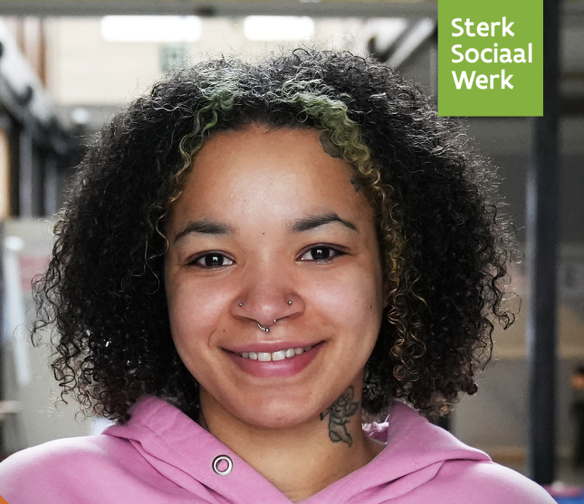 Person with curly hair and face piercings smiling, wearing a pink top. Background shows blurred indoor setting. "Sterk Sociaal Werk" logo visible.