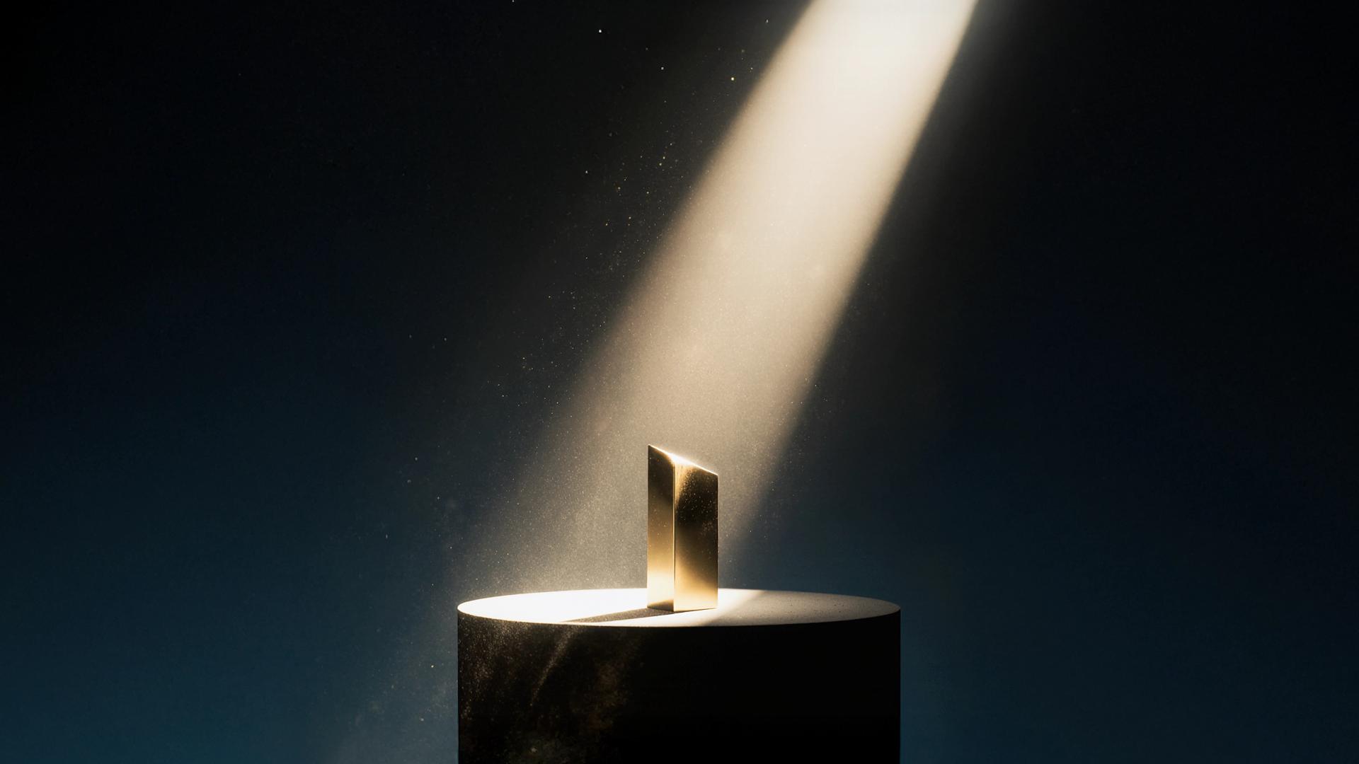 Golden award in spotlight on a dark cylindrical pedestal against a dark background, with light particles visible in the beam.