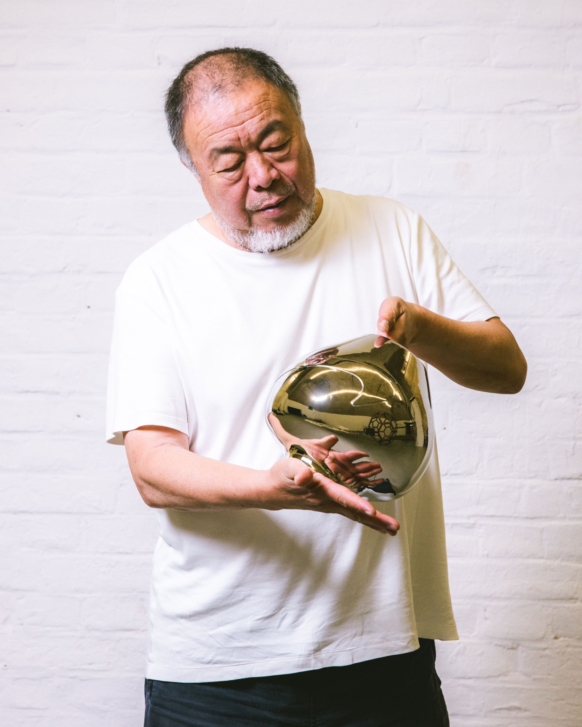 An image of artist Ai Weiwei holding a coloured metal vase sculpture.